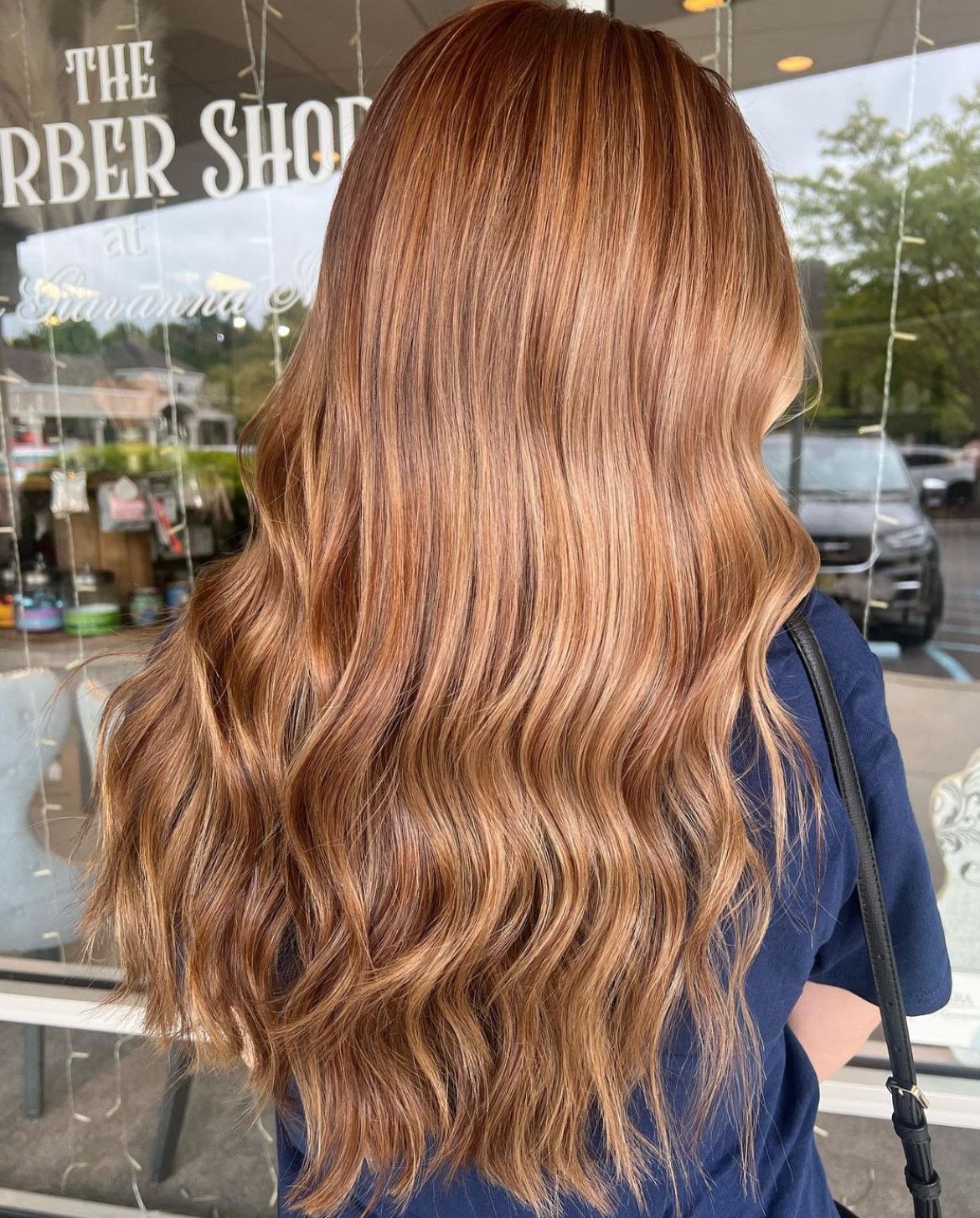 A woman with long brown hair is standing in front of a barber shop window.