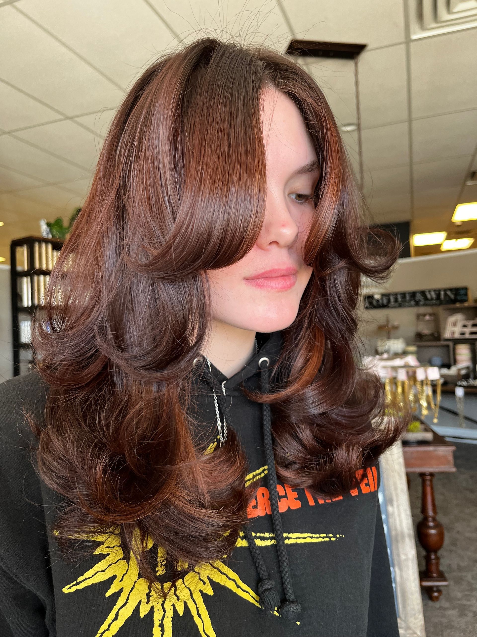 A woman with long brown hair is wearing a black shirt with a sun on it.