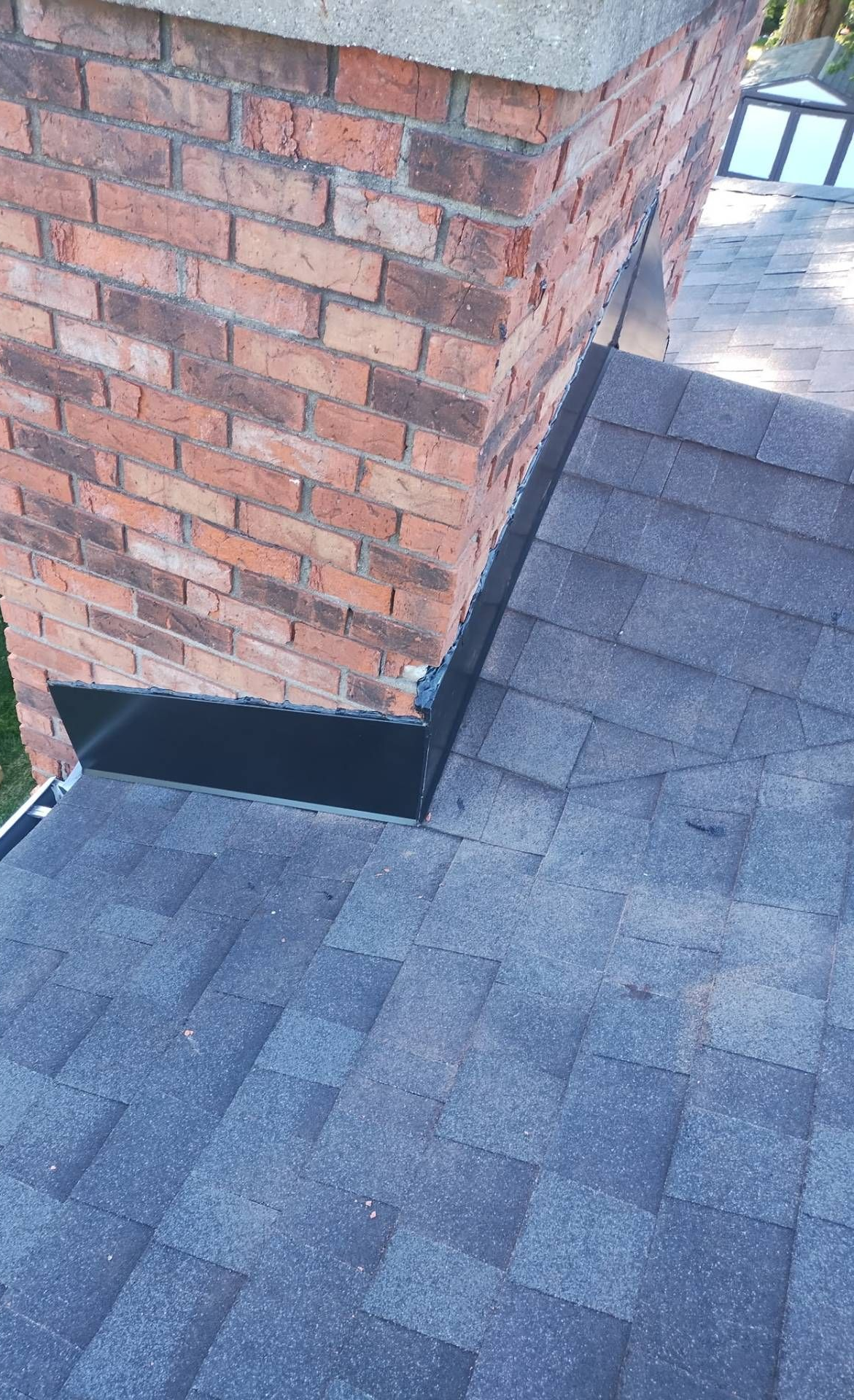 Brick chimney with black flashing on a dark shingle roof.