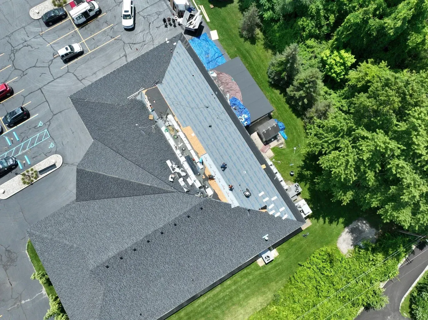 Aerial view of a building roof under construction with workers and parking lot.