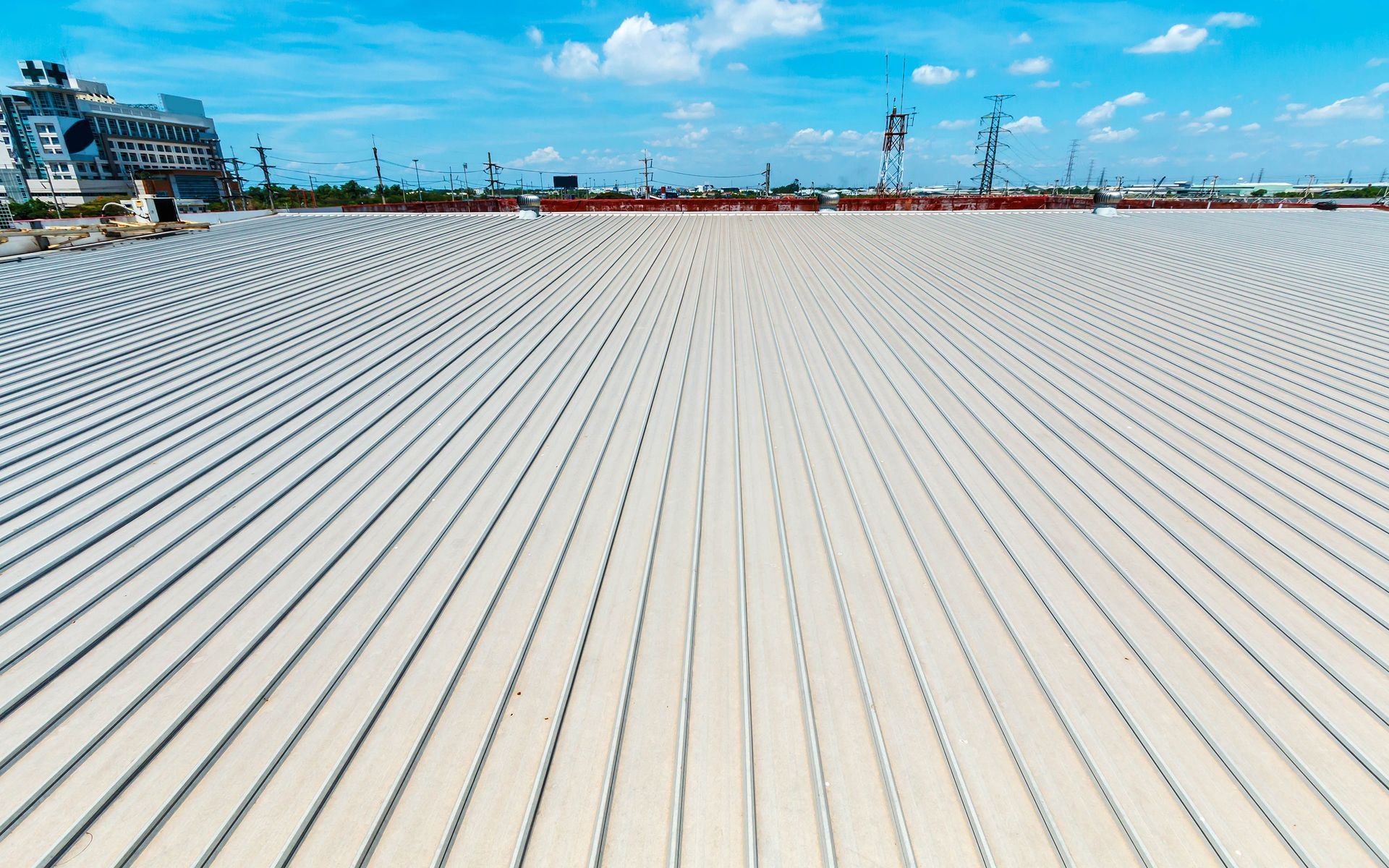 Rows of upright, gray concrete pillars stretch across a wide expanse, under a blue sky, near a building.