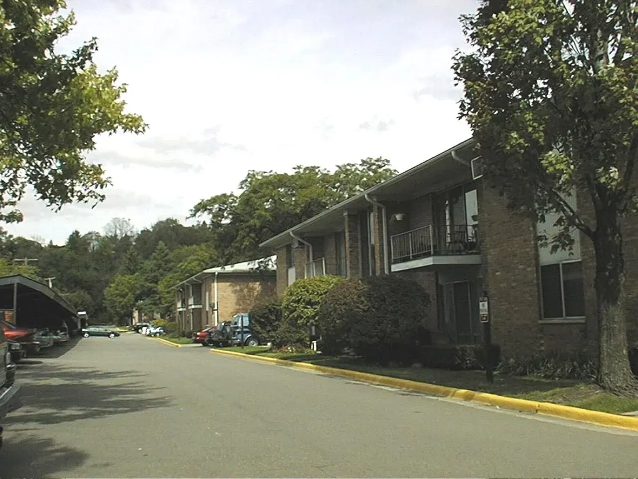 Apartment buildings with brick facade along a tree-lined street under a cloudy sky.