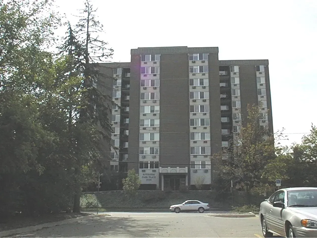 Gray apartment building with multiple stories, windows, and parked cars in front.