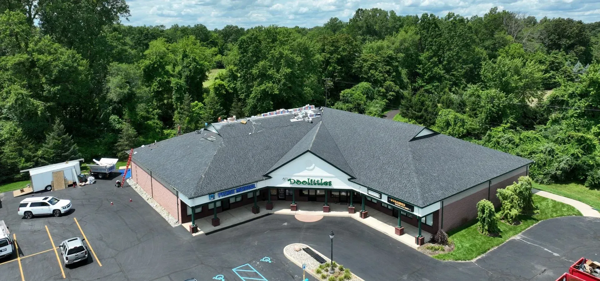 Aerial view of a business with a black roof, surrounded by trees and a parking lot.