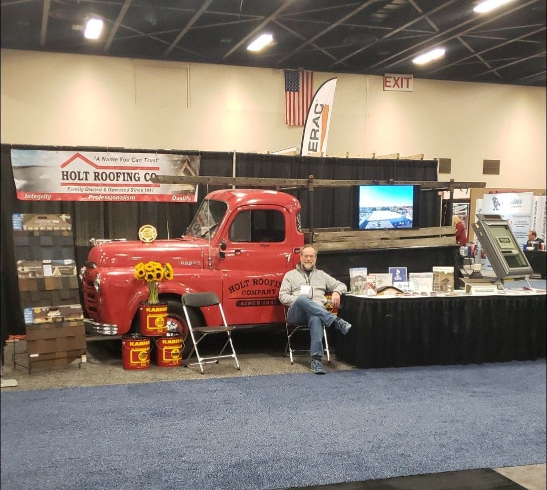 Red truck and man at a booth for Bolt Roofing Co. in front of a US flag and ERAG sign.