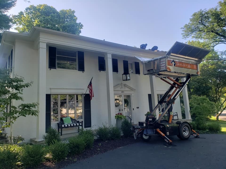 White house with workers on roof, orange lift equipment, American flag, sunny day.