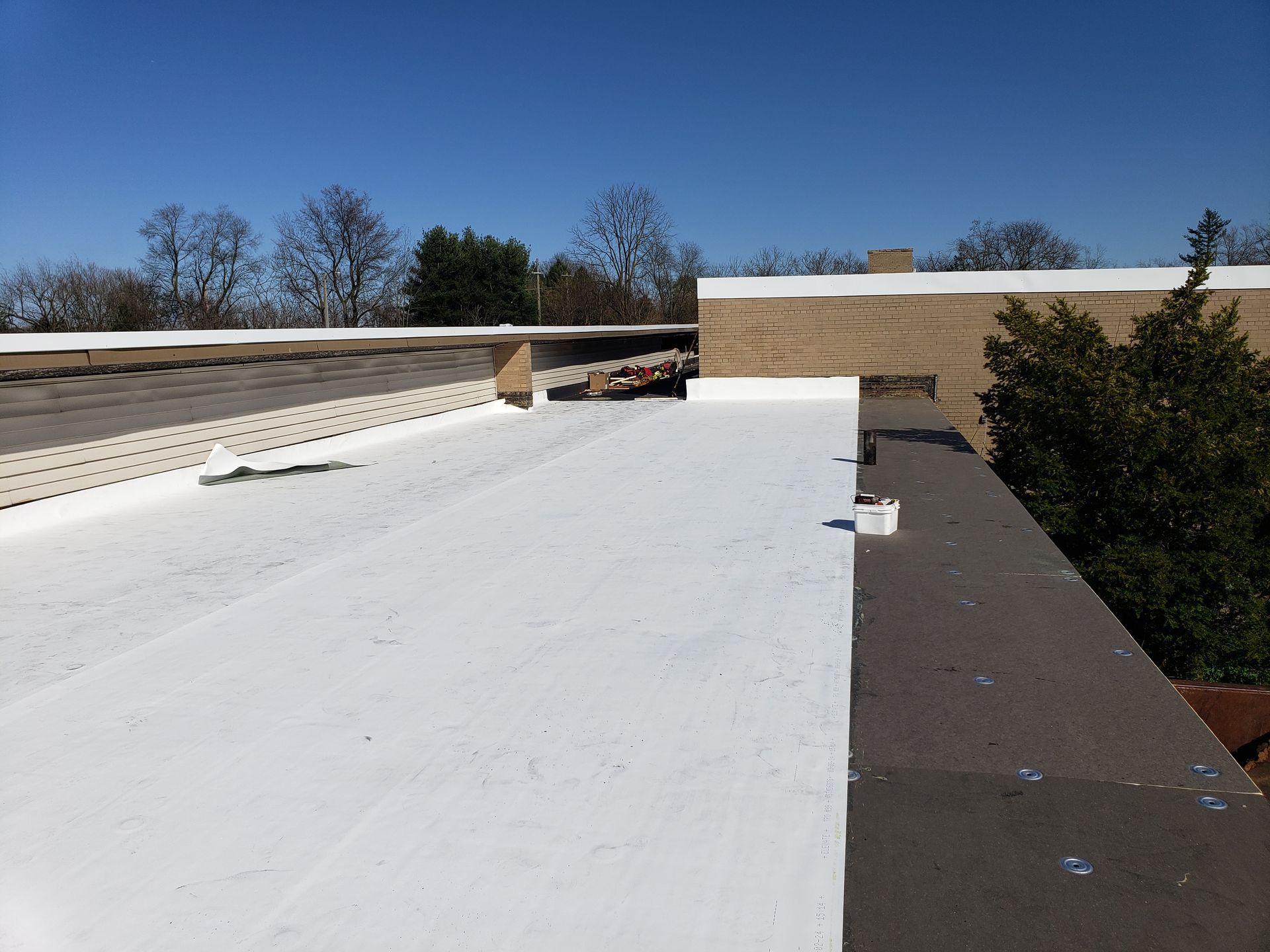 Two men are working on a roof and a shovel is laying on the ground.