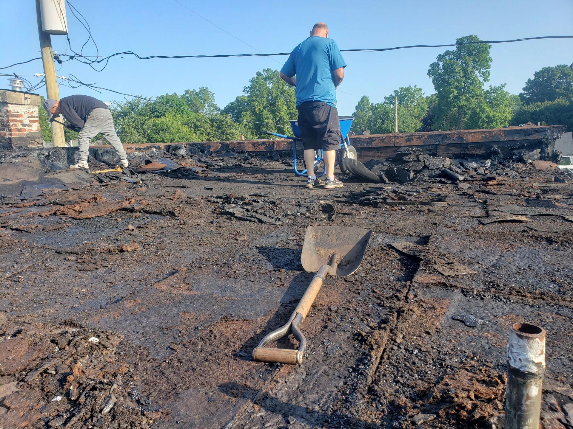 Two men are working on a roof and a shovel is laying on the ground.