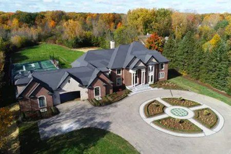 an aerial view of a large brick house with a large driveway surrounded by trees .