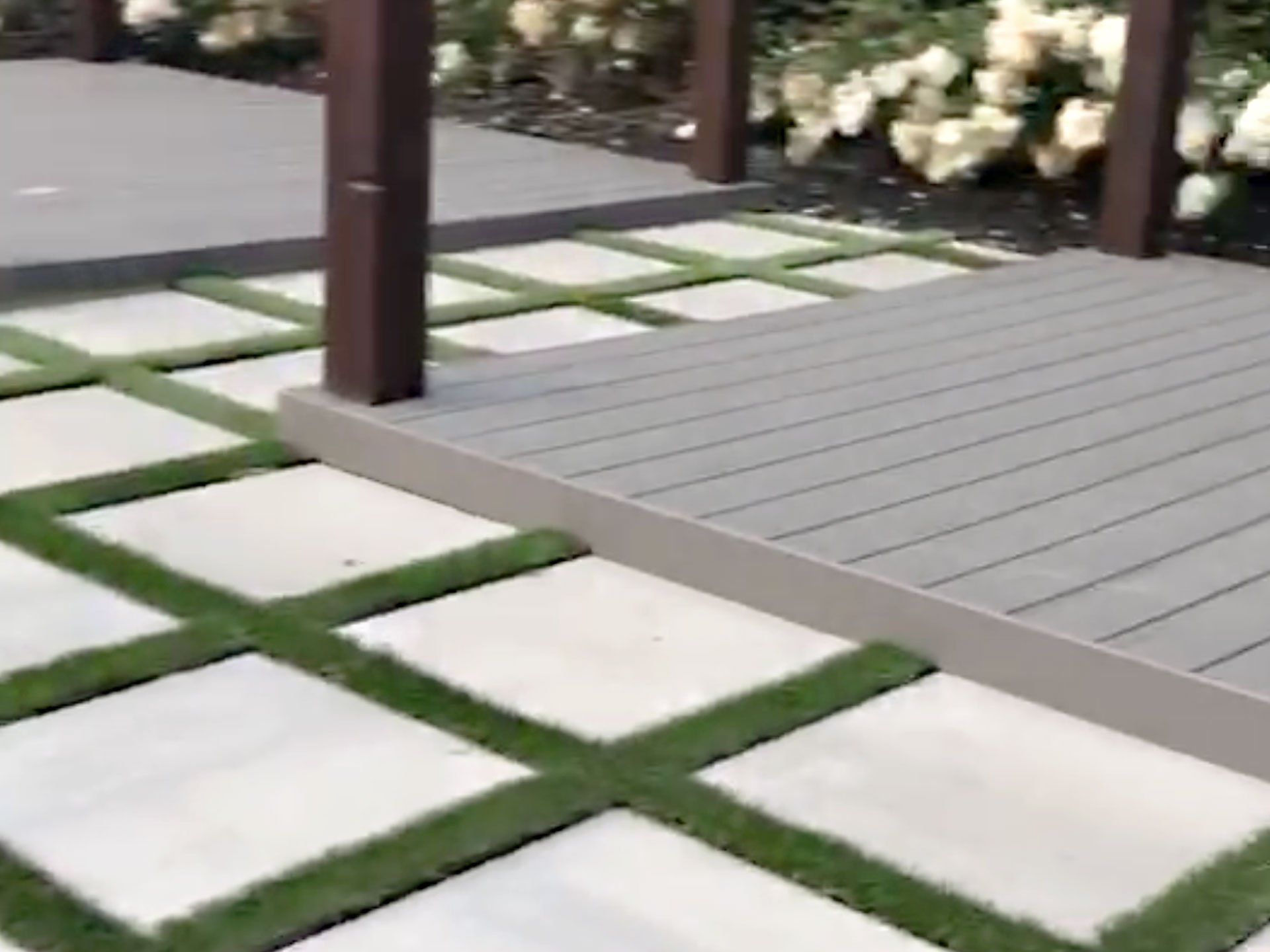 A patio with a wooden deck and a concrete walkway with grass.
