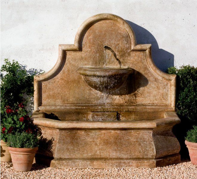 a large stone fountain is surrounded by potted plants and gravel