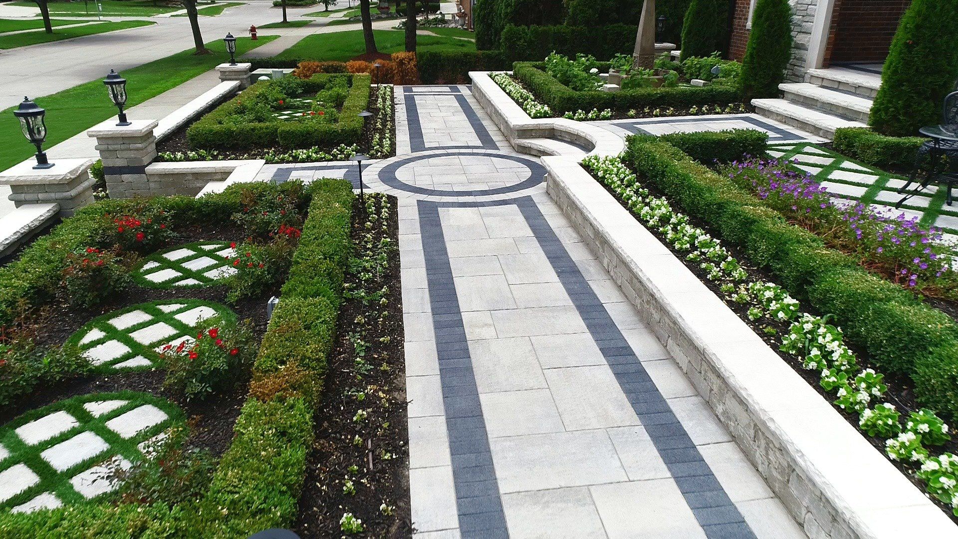 A brick walkway leading to a house surrounded by bushes and flowers