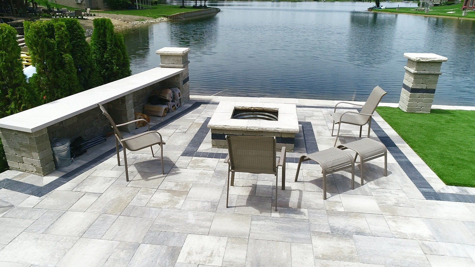 A patio with a fire pit and chairs in front of a lake.