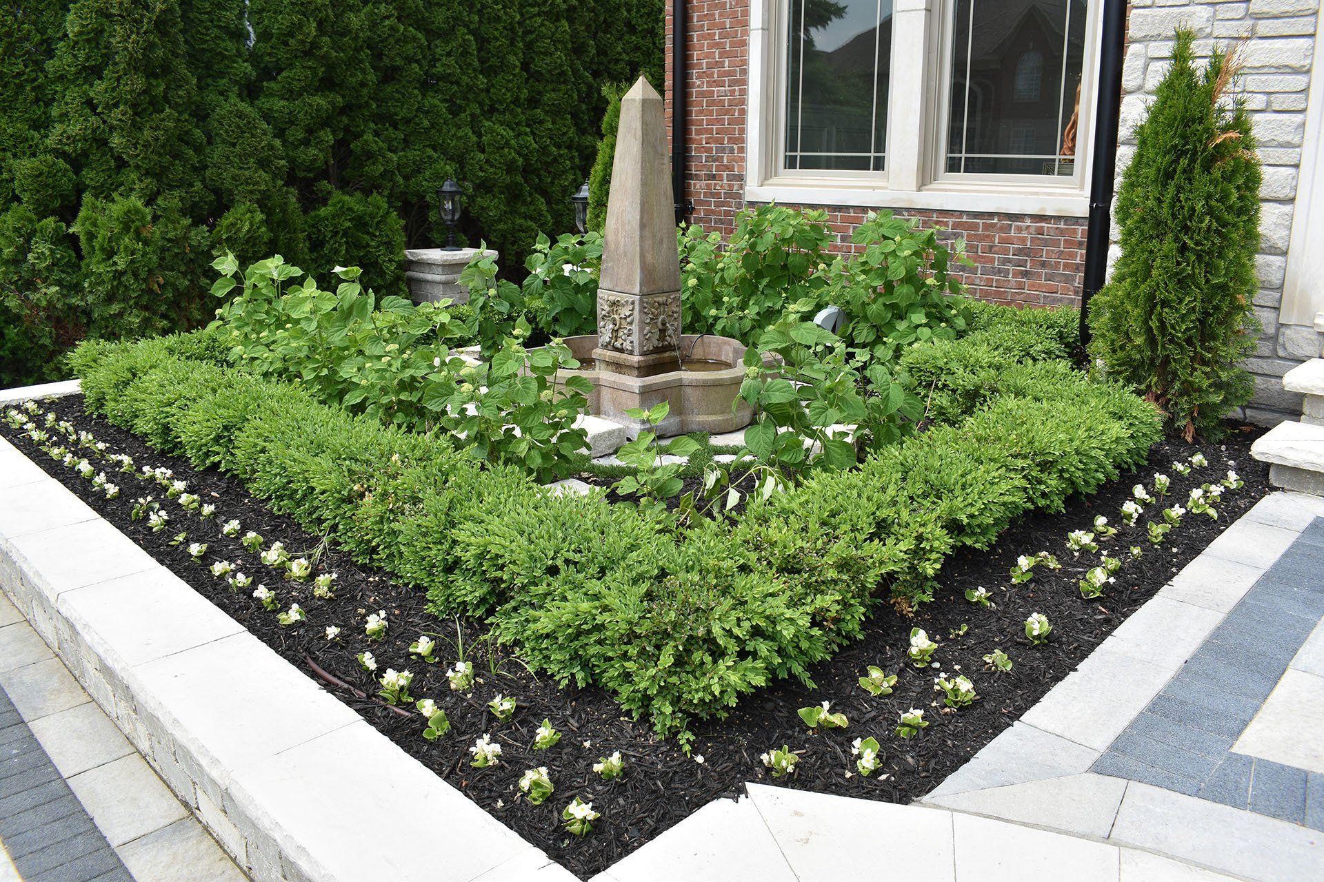 A garden with a fountain in the middle of it in front of a brick house.
