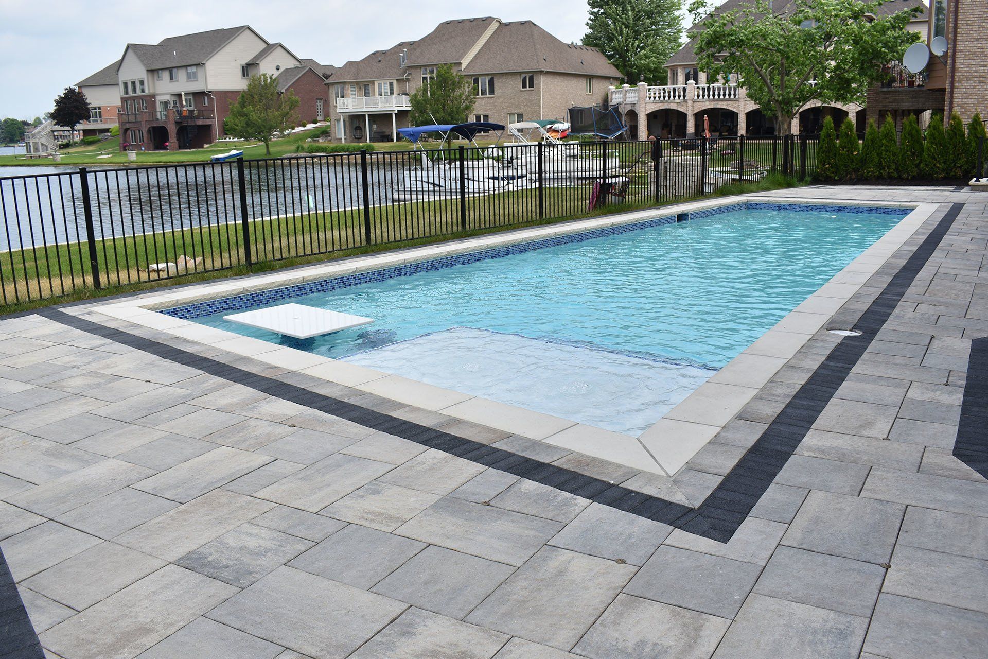 A large swimming pool is surrounded by a fence and a patio.