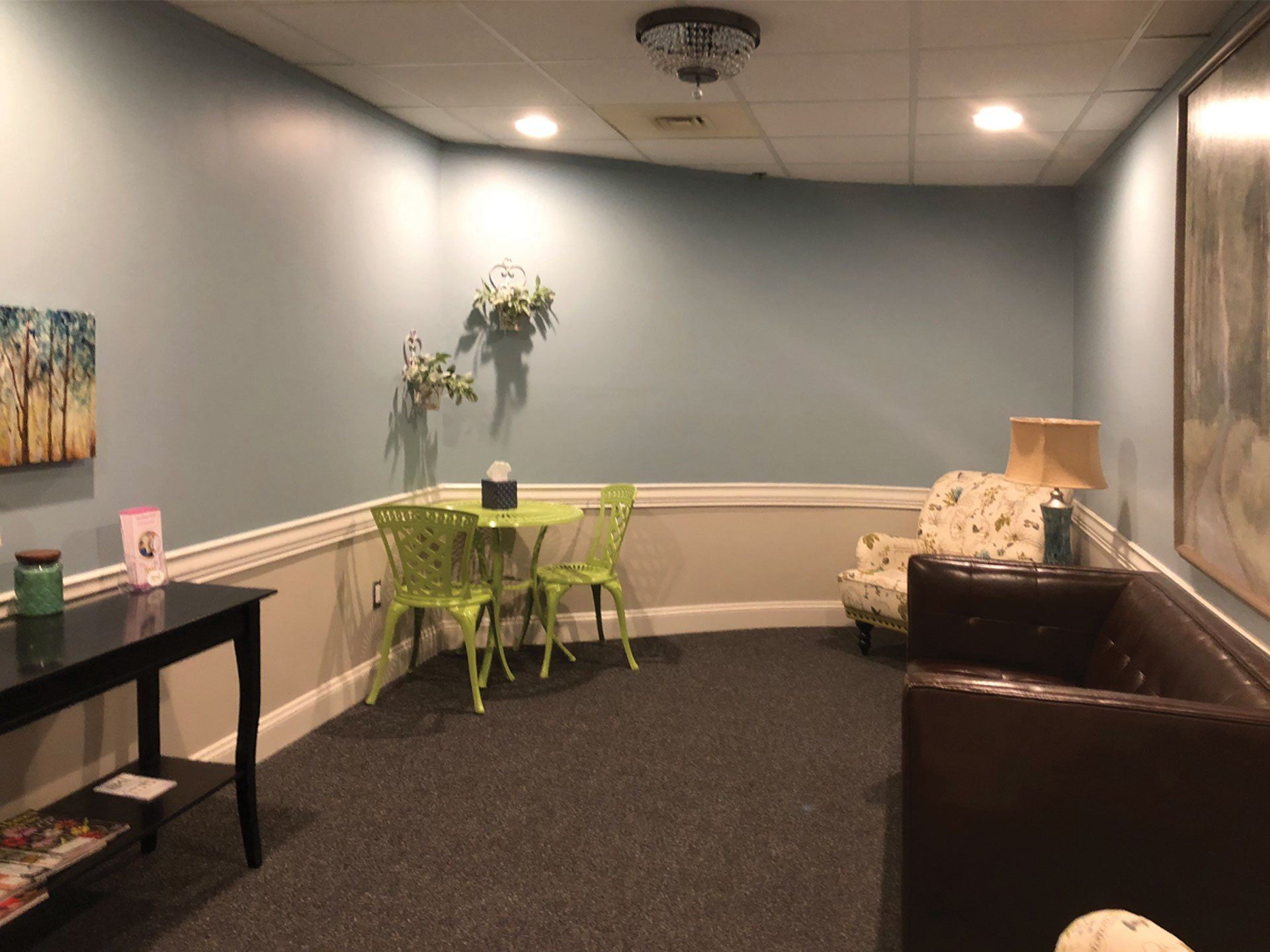 A waiting room with a couch , chairs , table and lamp.