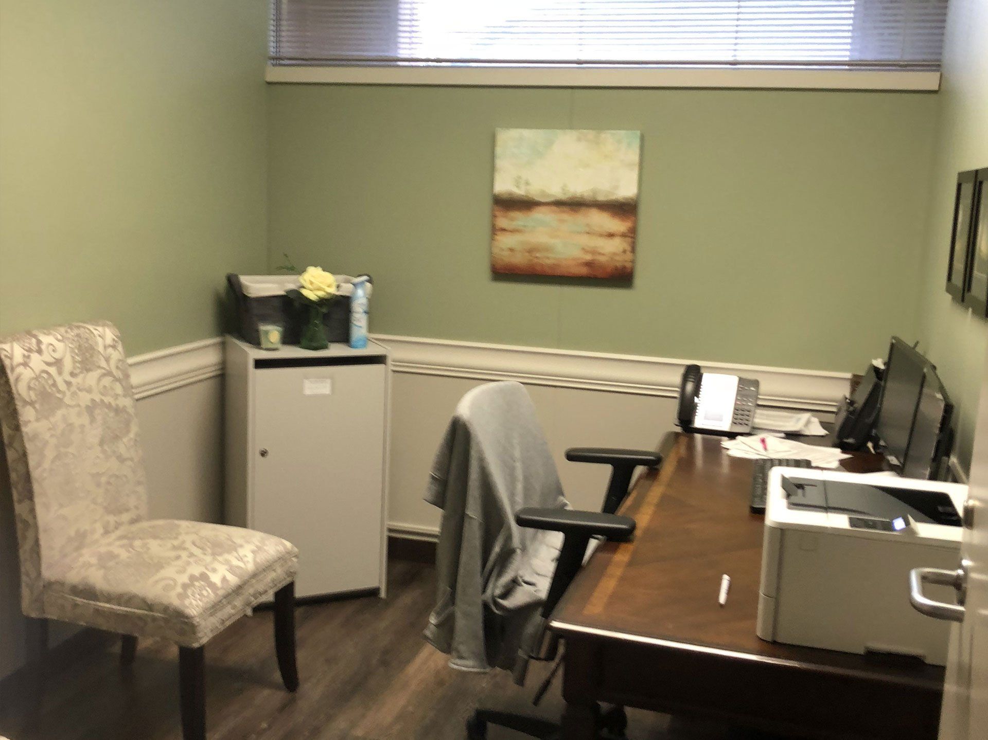 A small office with a desk , chair , printer and computer.