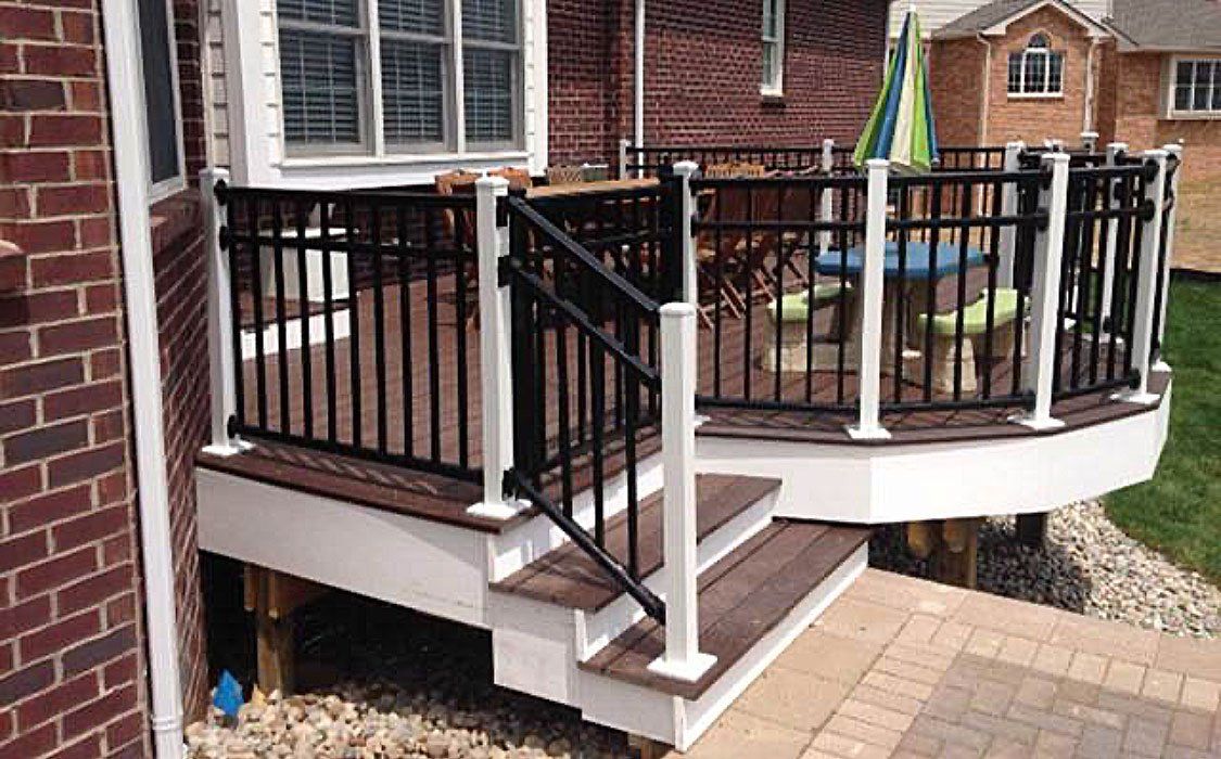 A deck with stairs and a black railing in front of a brick house.