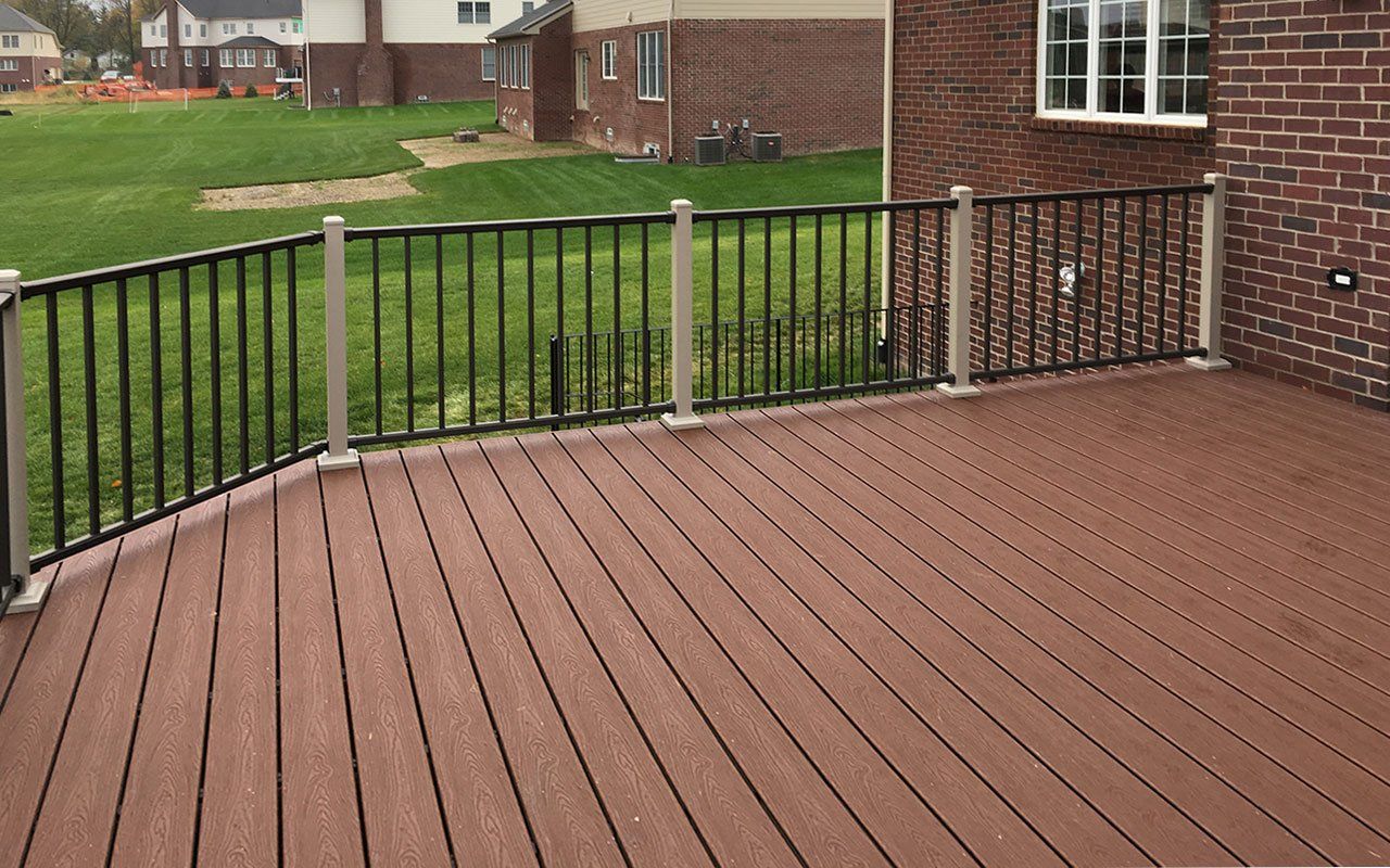 a wooden deck with a metal railing and a brick house in the background .