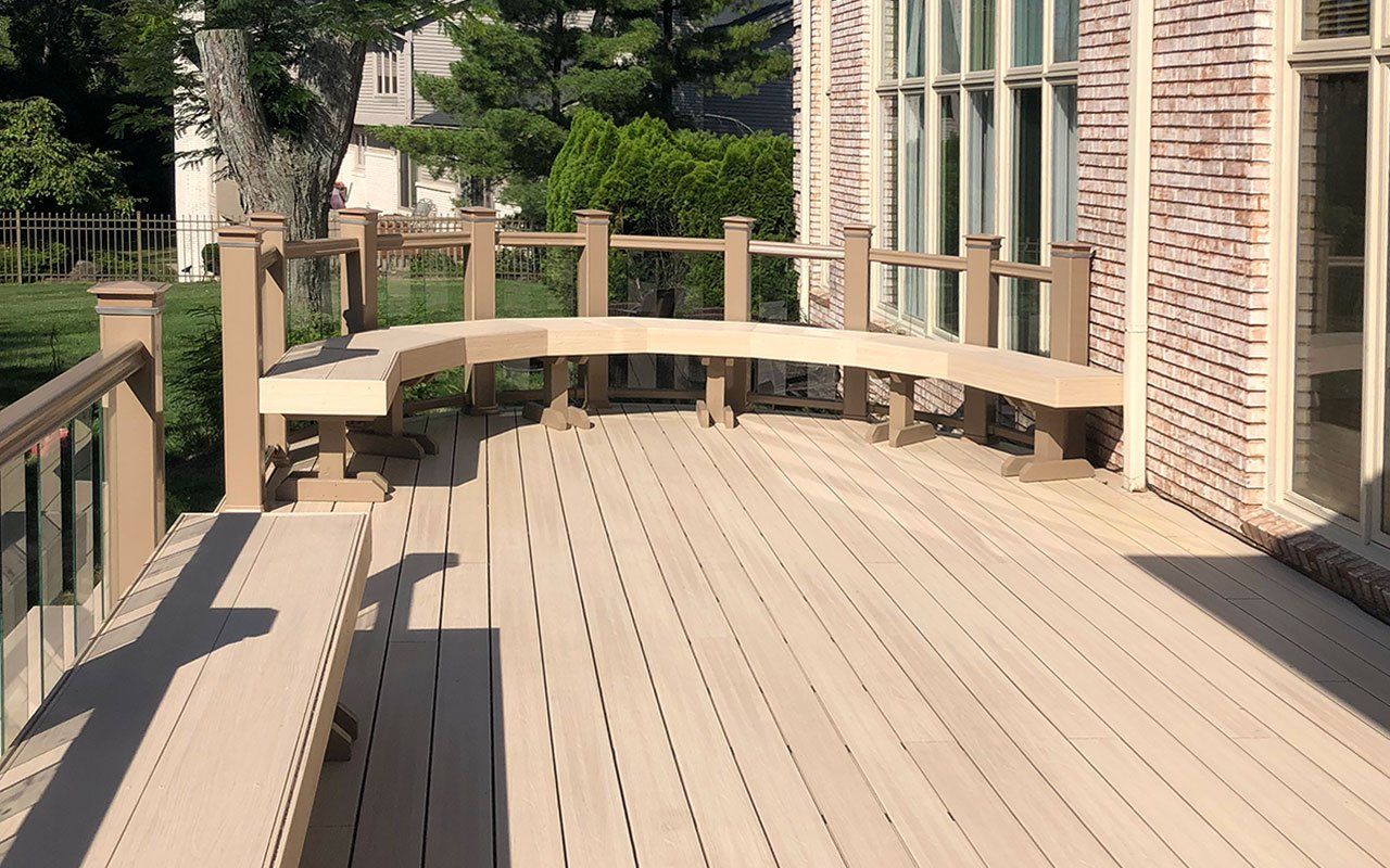 a wooden deck with a curved bench and a brick building in the background .