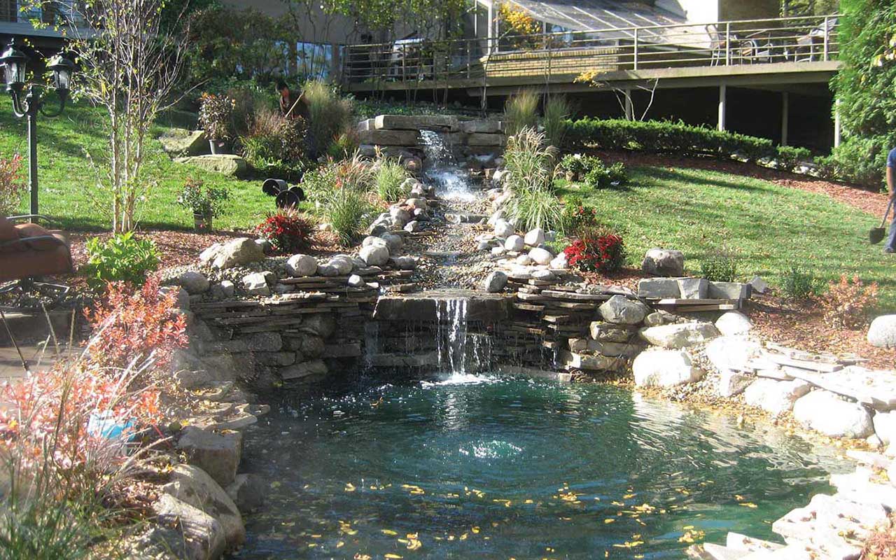A waterfall in a garden with a house in the background