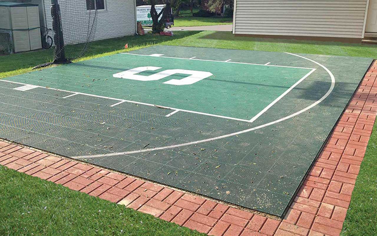 A basketball court in a backyard with a brick walkway.