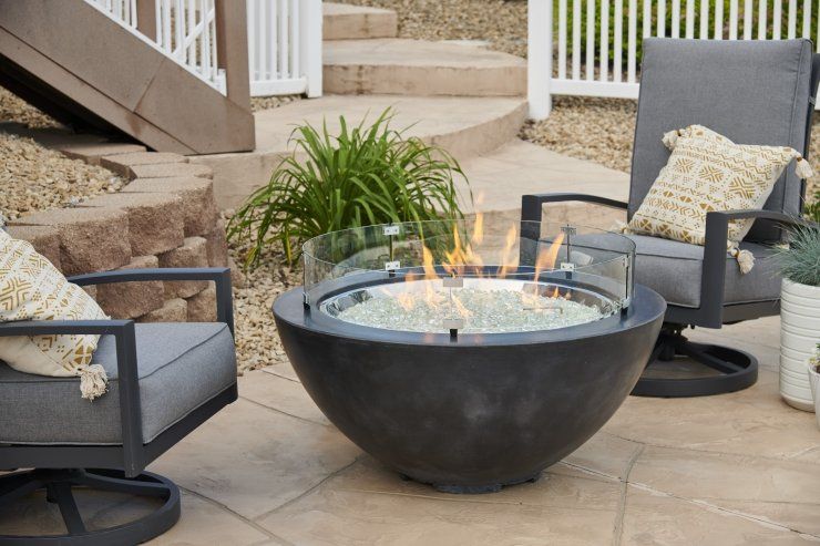 a fire pit is sitting on a patio next to two chairs .