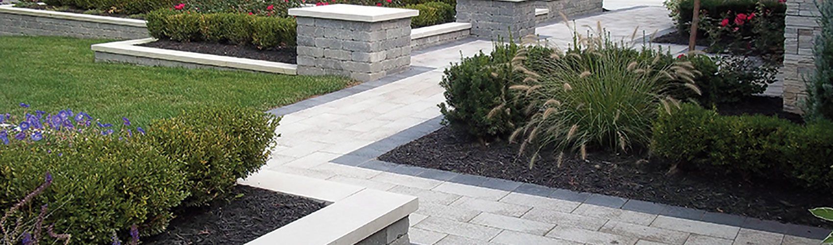 a brick walkway leading to a house surrounded by bushes and flowers .
