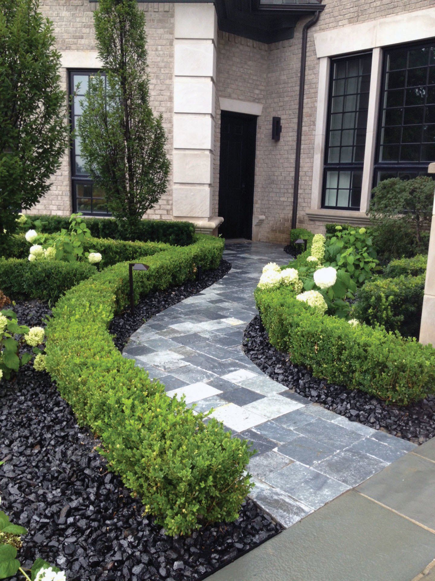 a brick house with a walkway leading to the front door surrounded by bushes and flowers .