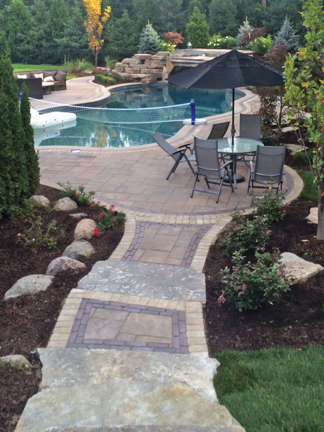 a patio with a table and chairs and an umbrella next to a pool