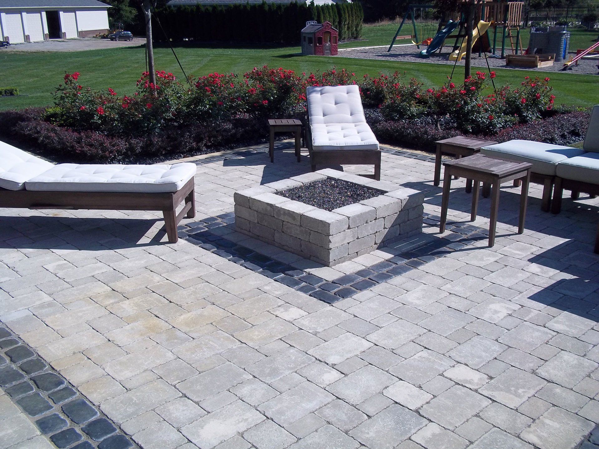 a patio with a fire pit and lounge chairs