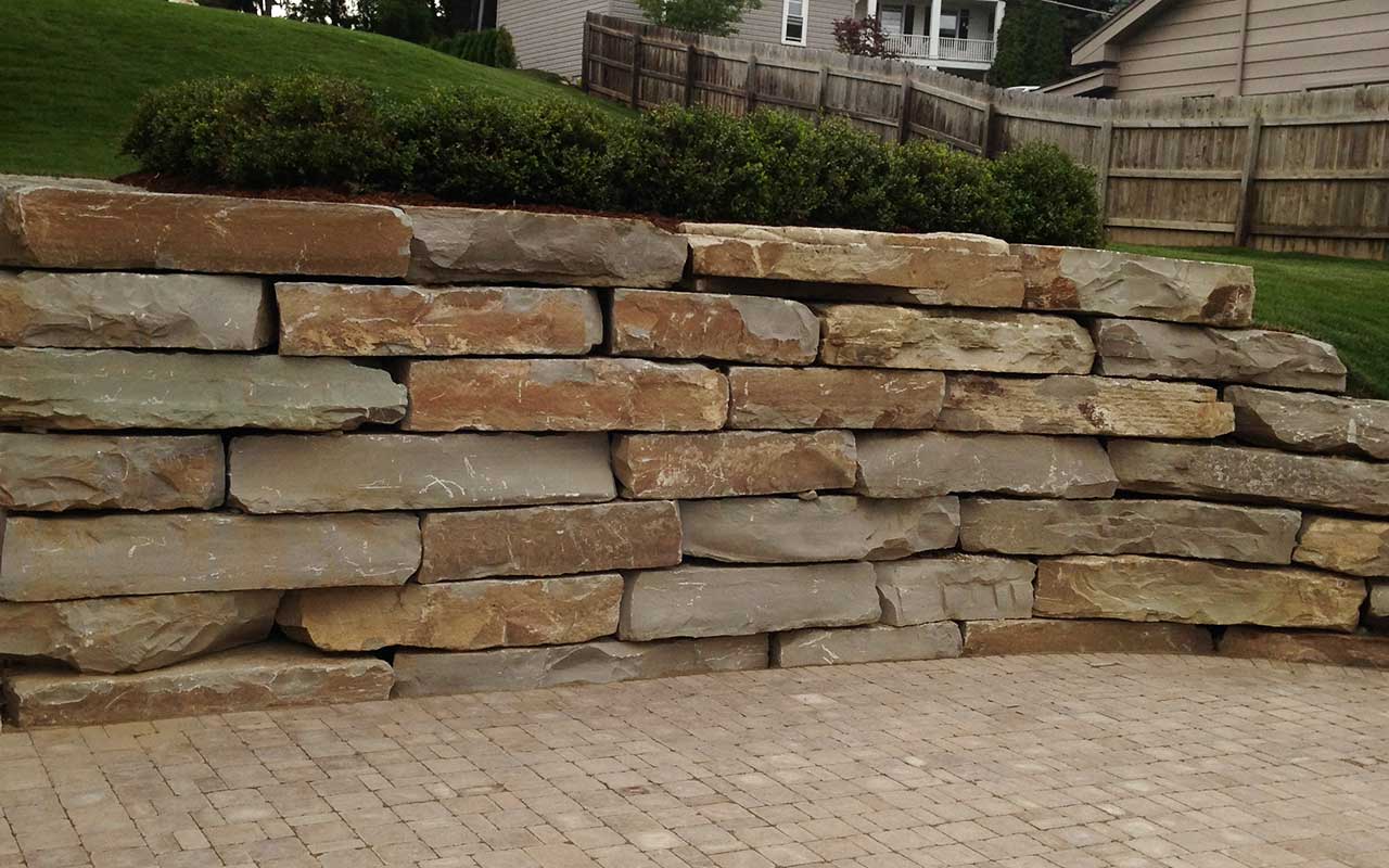 a large stone wall is sitting on top of a brick driveway .