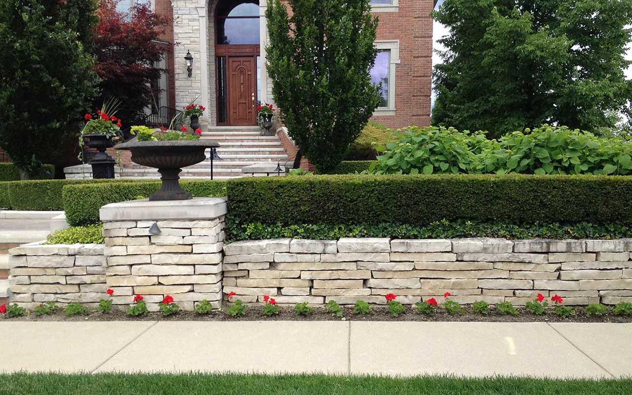 a stone wall surrounds a lush green lawn in front of a brick house .