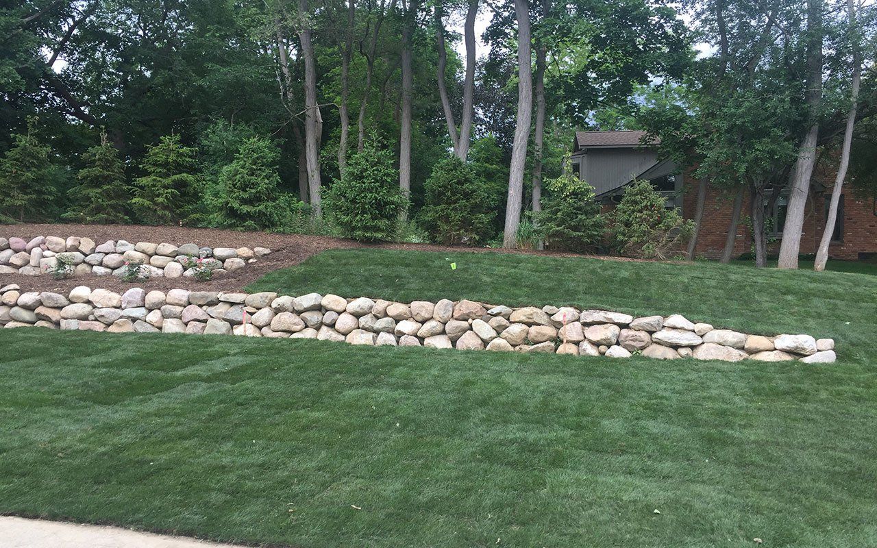 a lush green lawn with a stone wall and trees in the background .