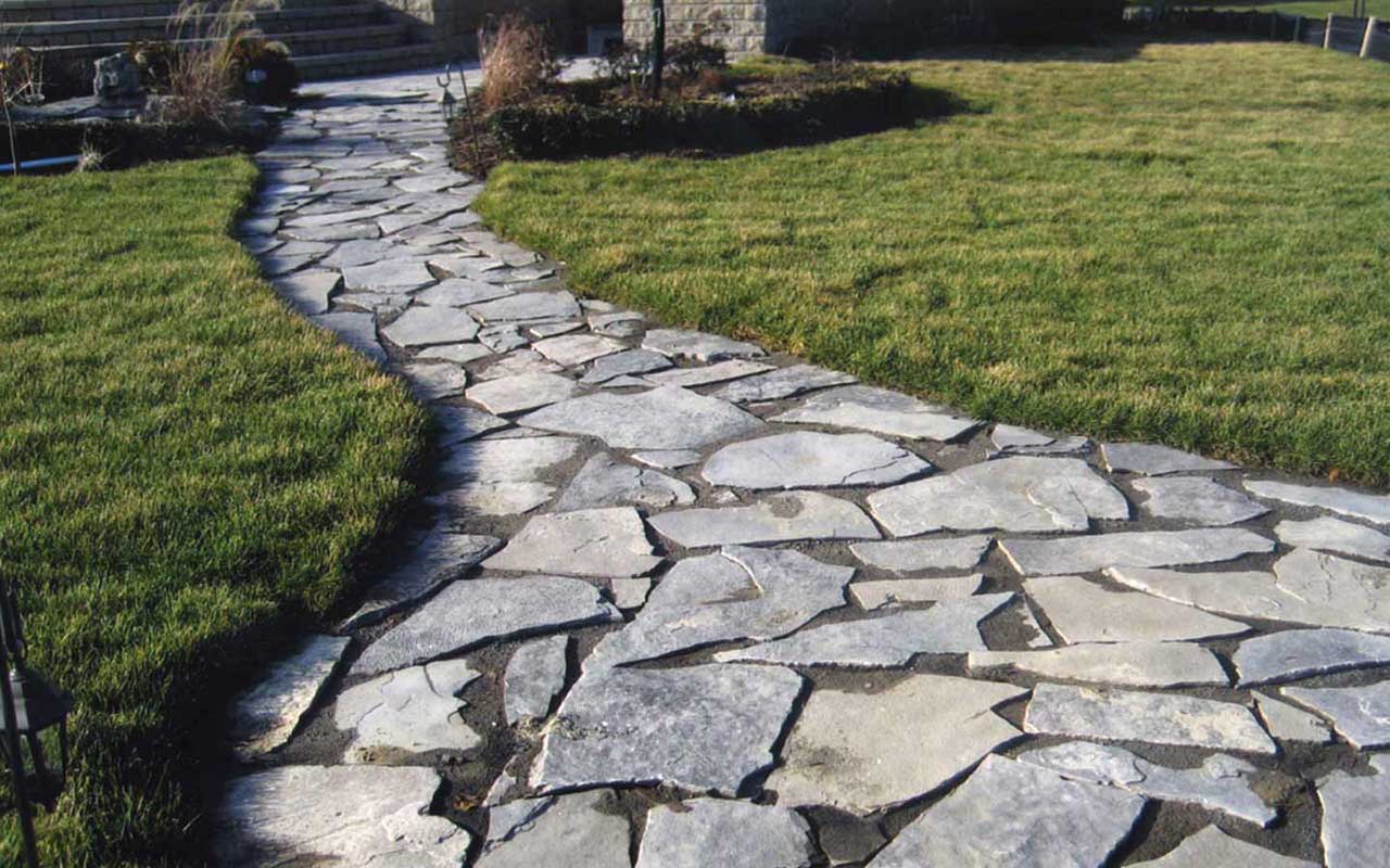 a stone walkway going through a lush green field