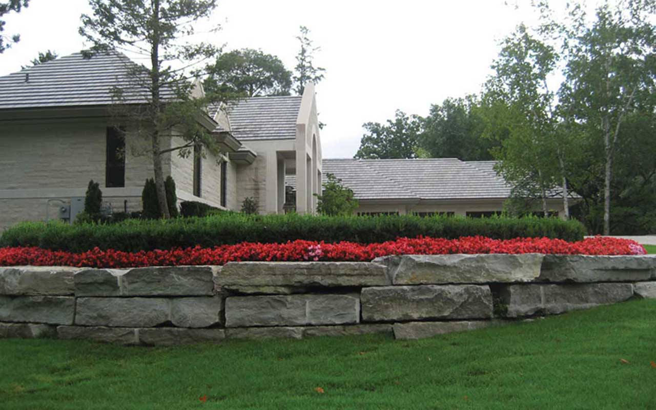 a stone wall with red flowers in front of a house