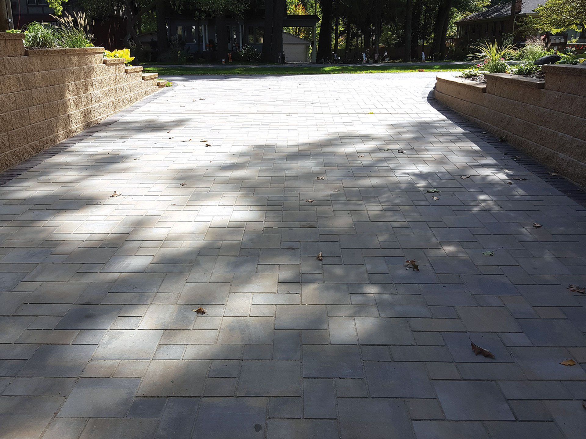 a brick driveway leading to a house with trees in the background