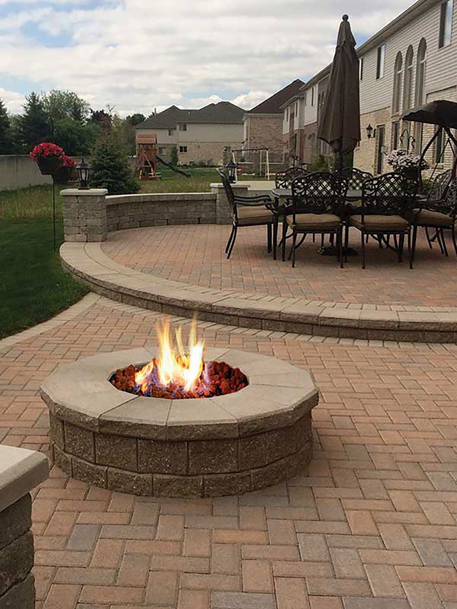 a fire pit is sitting on a brick patio next to a dining table and chairs .