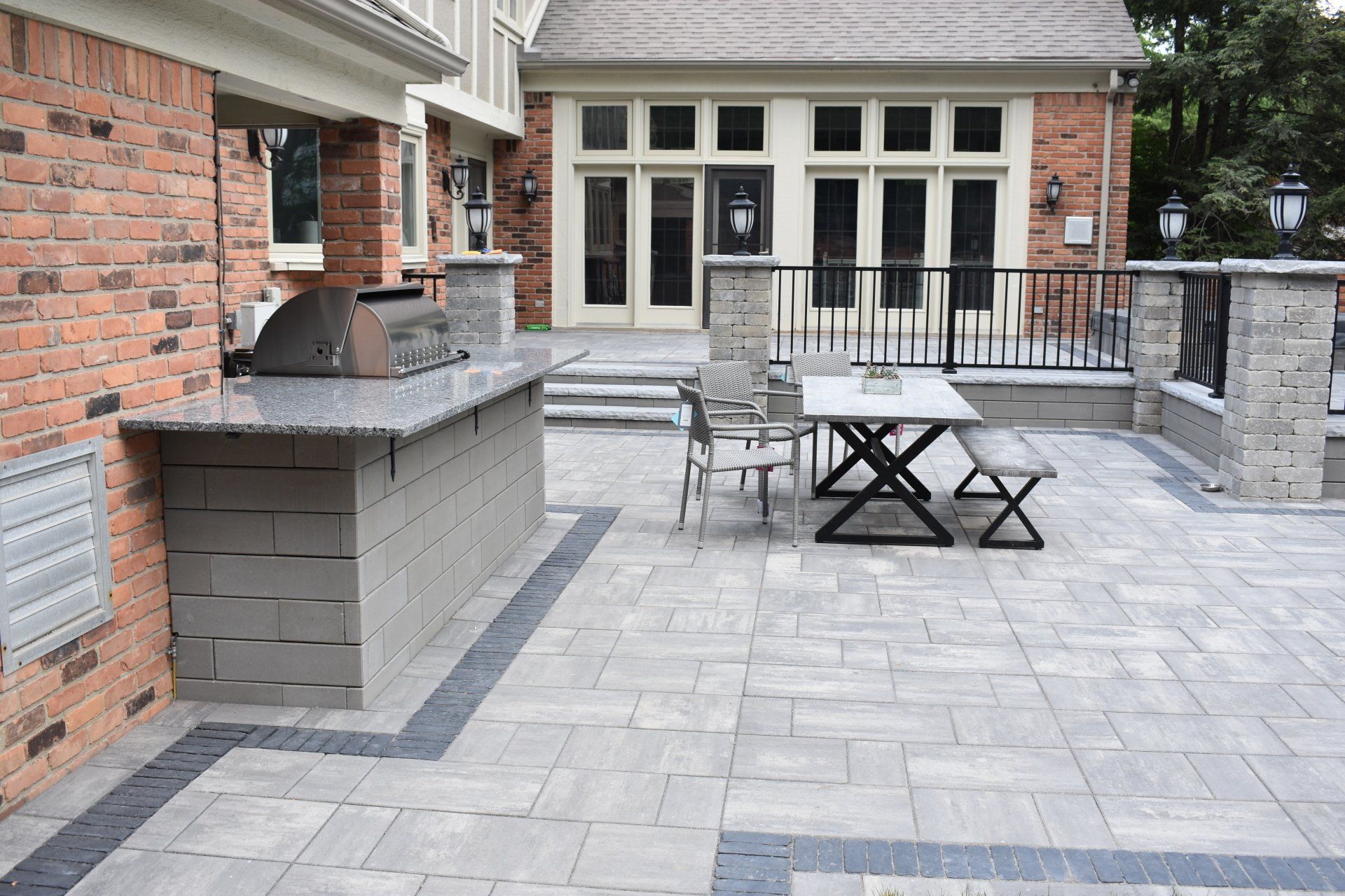A patio with a grill , table and chairs in front of a brick house.
