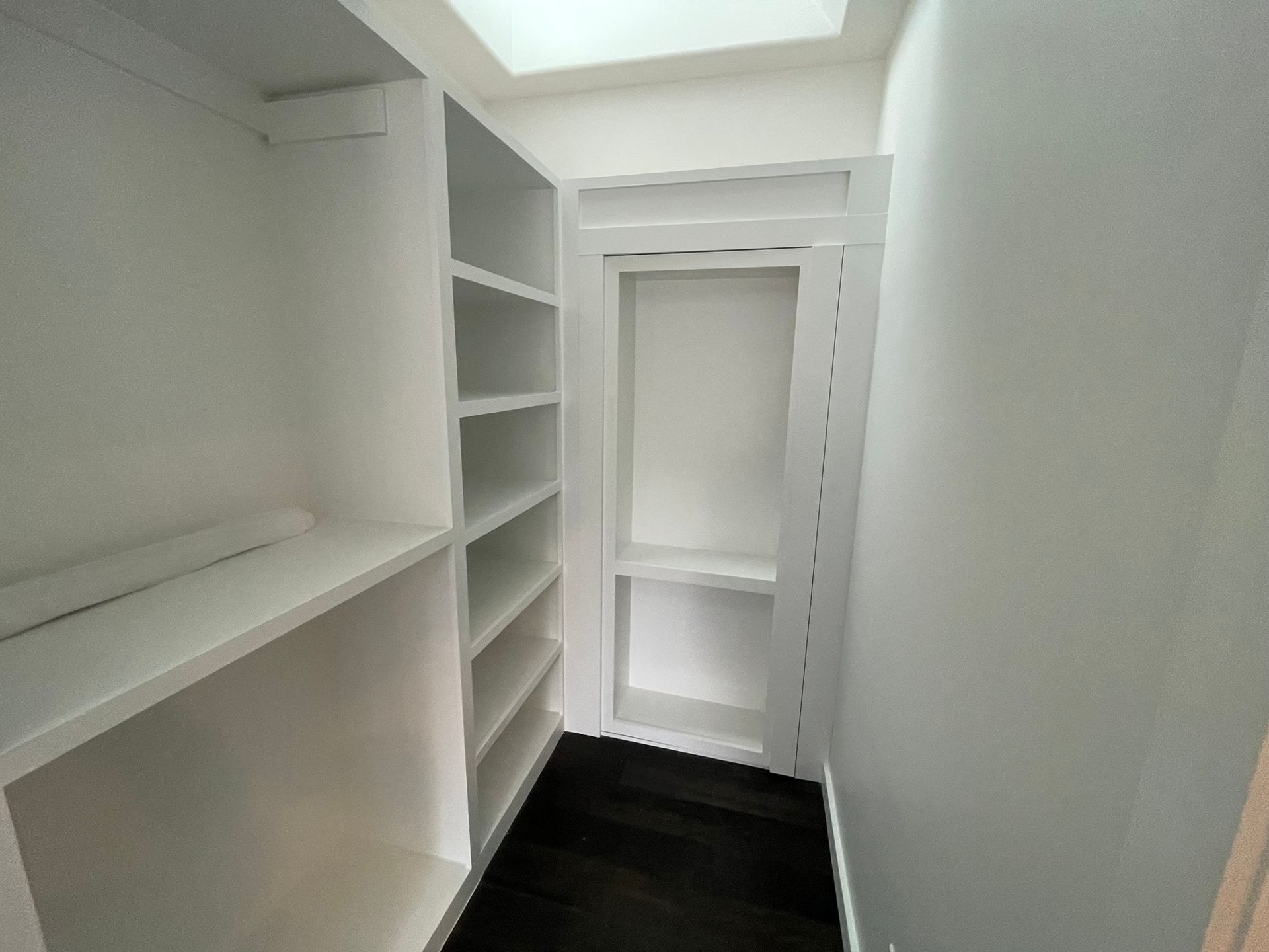 A walk in closet with lots of shelves and a skylight.