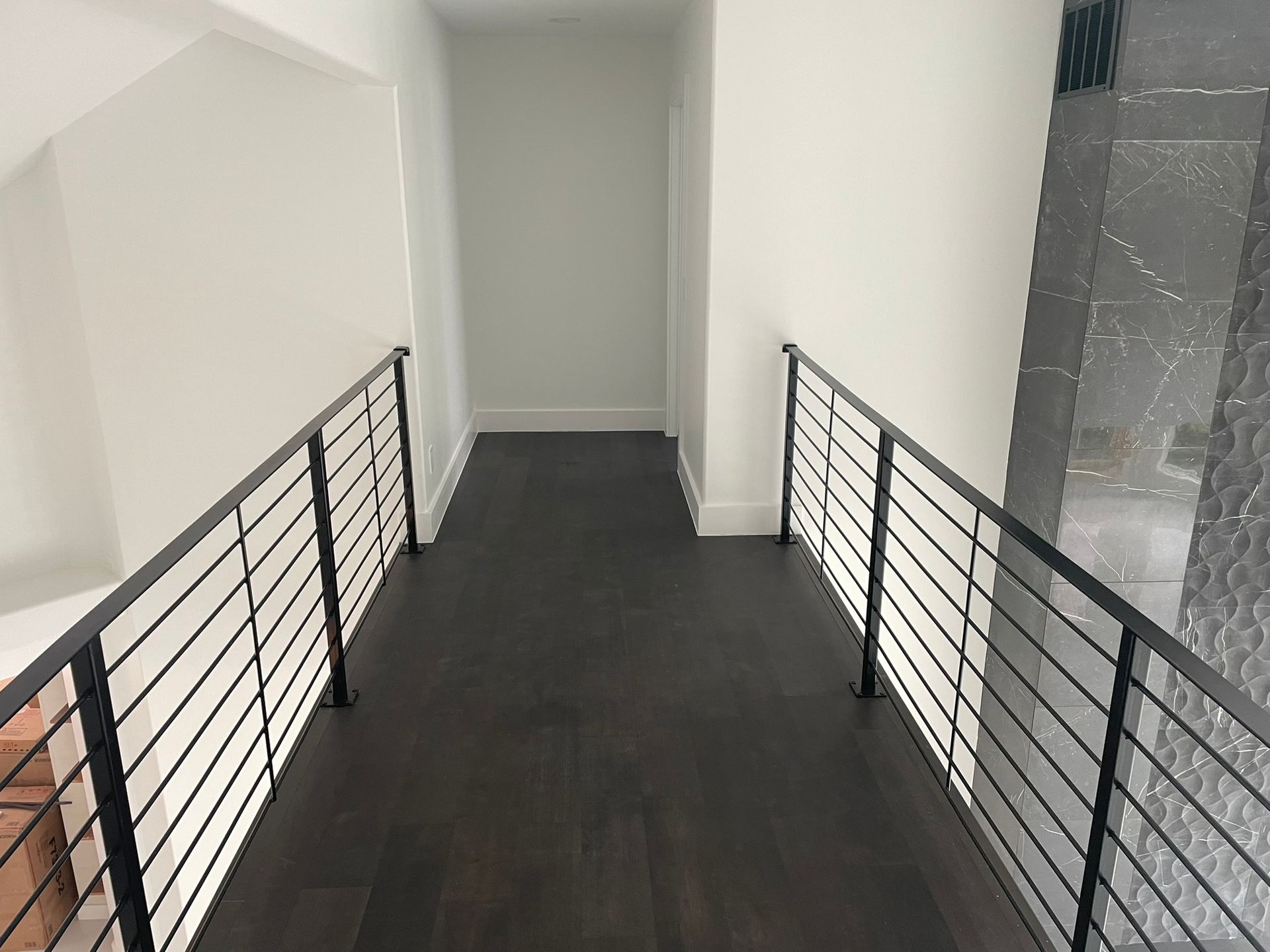 A hallway with a black railing leading to a staircase.