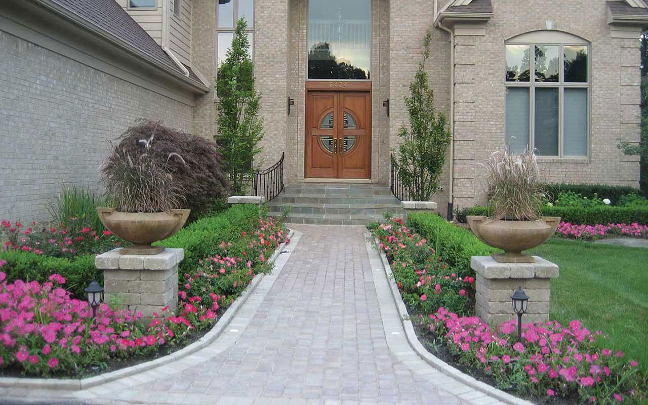 a brick walkway leading to the front door of a house surrounded by pink flowers .