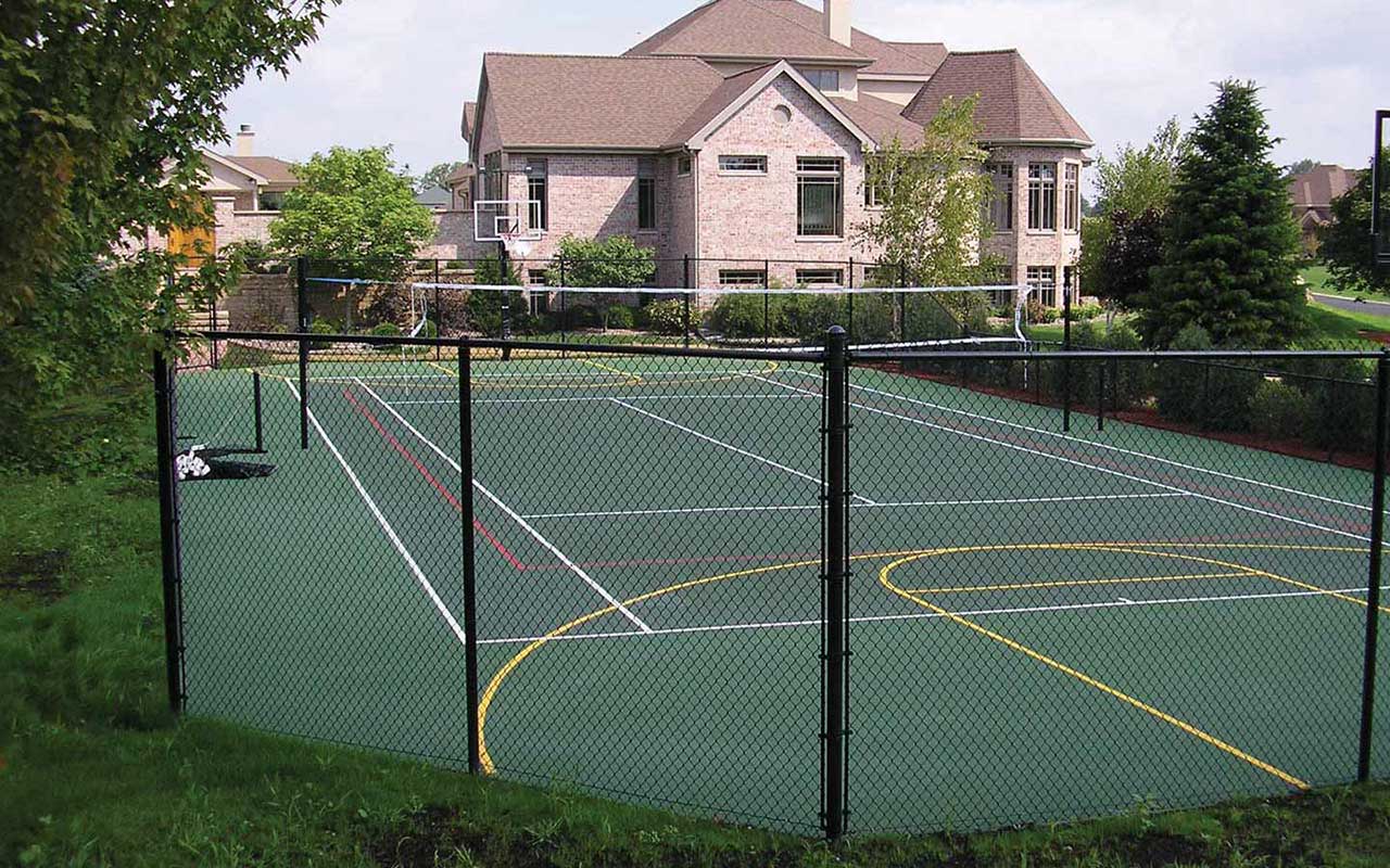 a tennis court behind a chain link fence with a large house in the background
