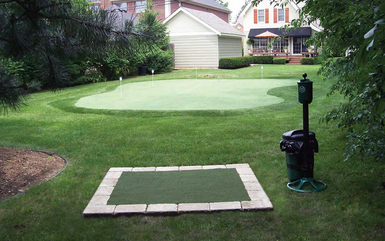 a backyard with a putting green and a trash can
