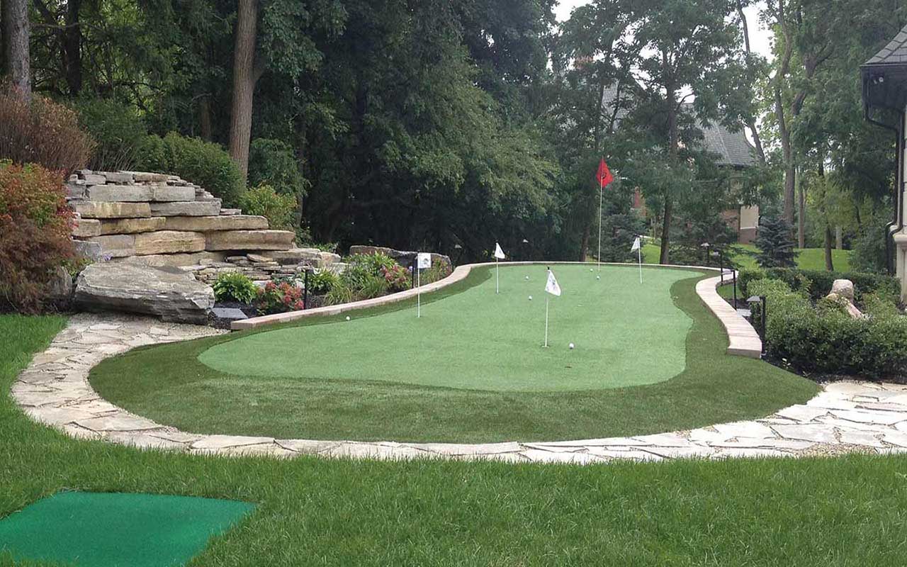 a putting green in a backyard with a stone walkway leading to it .