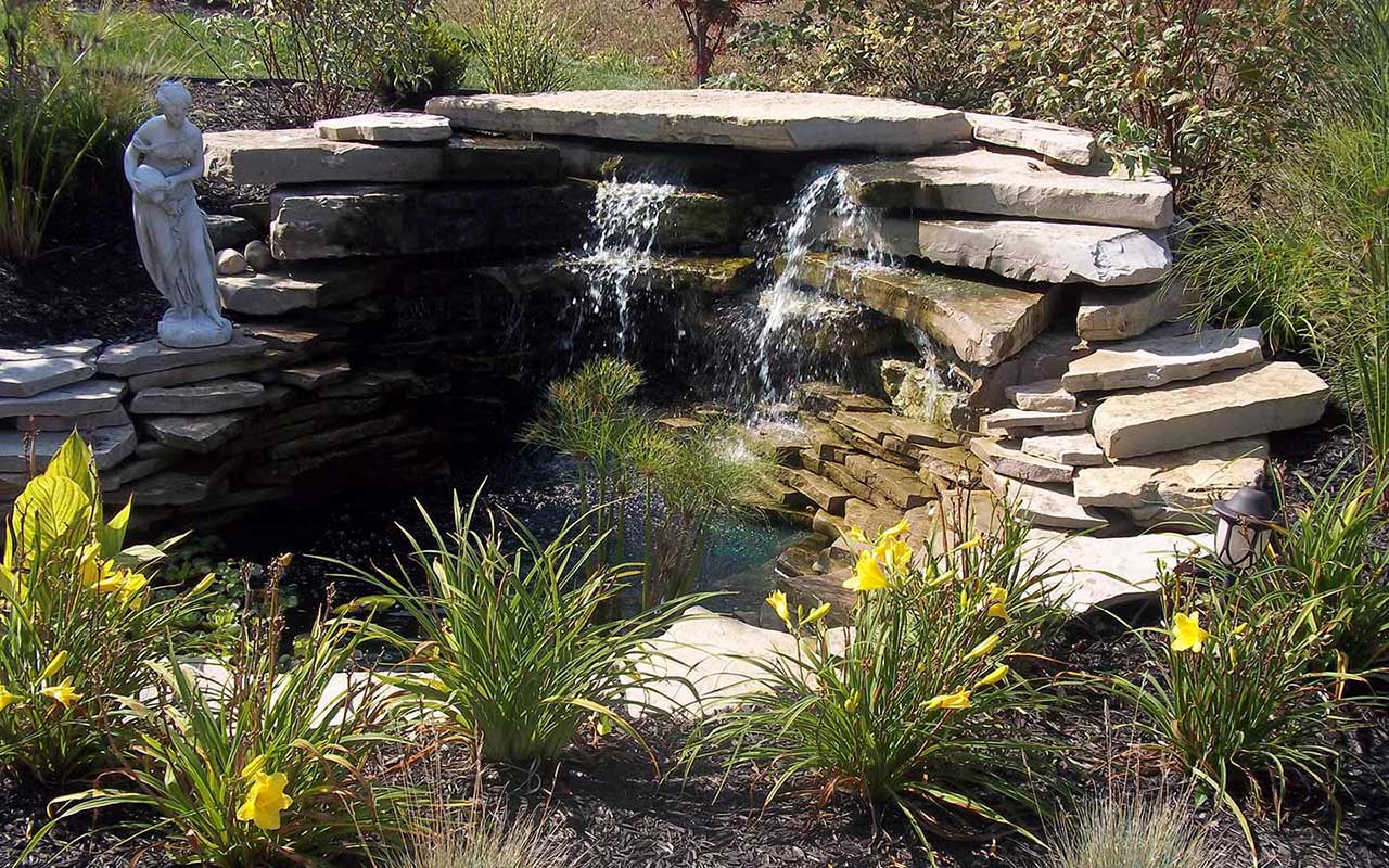 a waterfall in a garden with a statue in the background