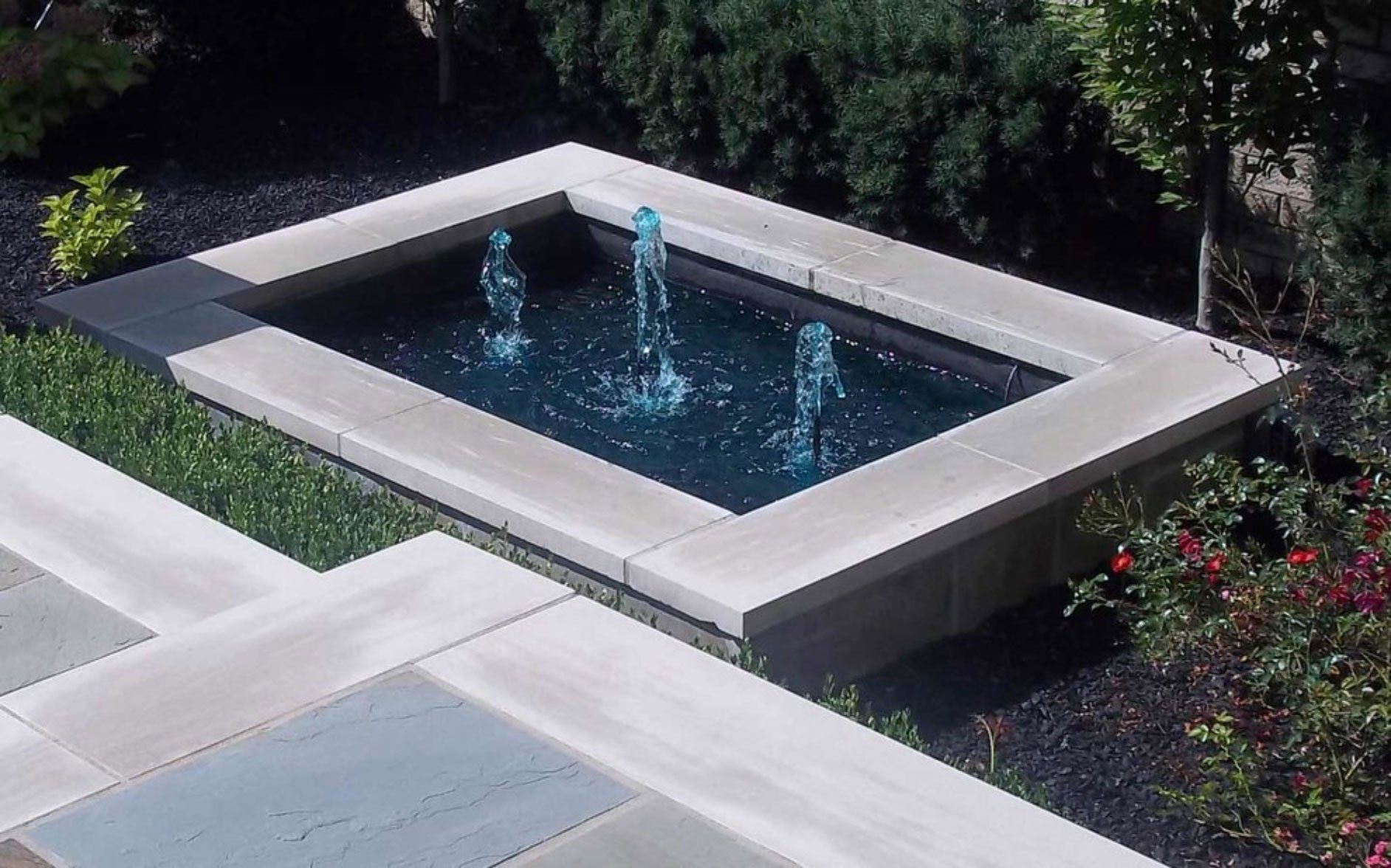 a fountain in the middle of a garden with trees in the background