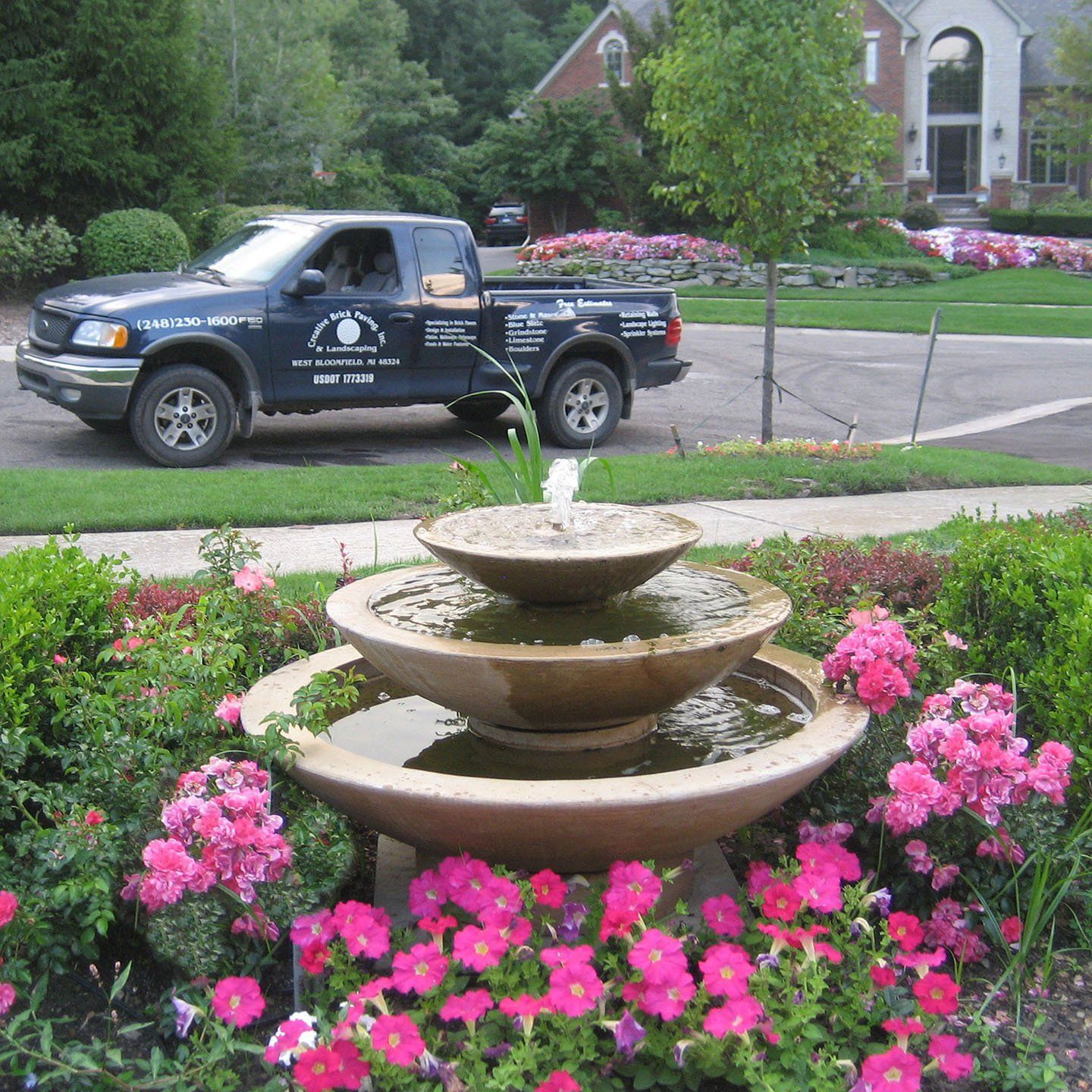 a truck is parked in front of a fountain surrounded by pink flowers