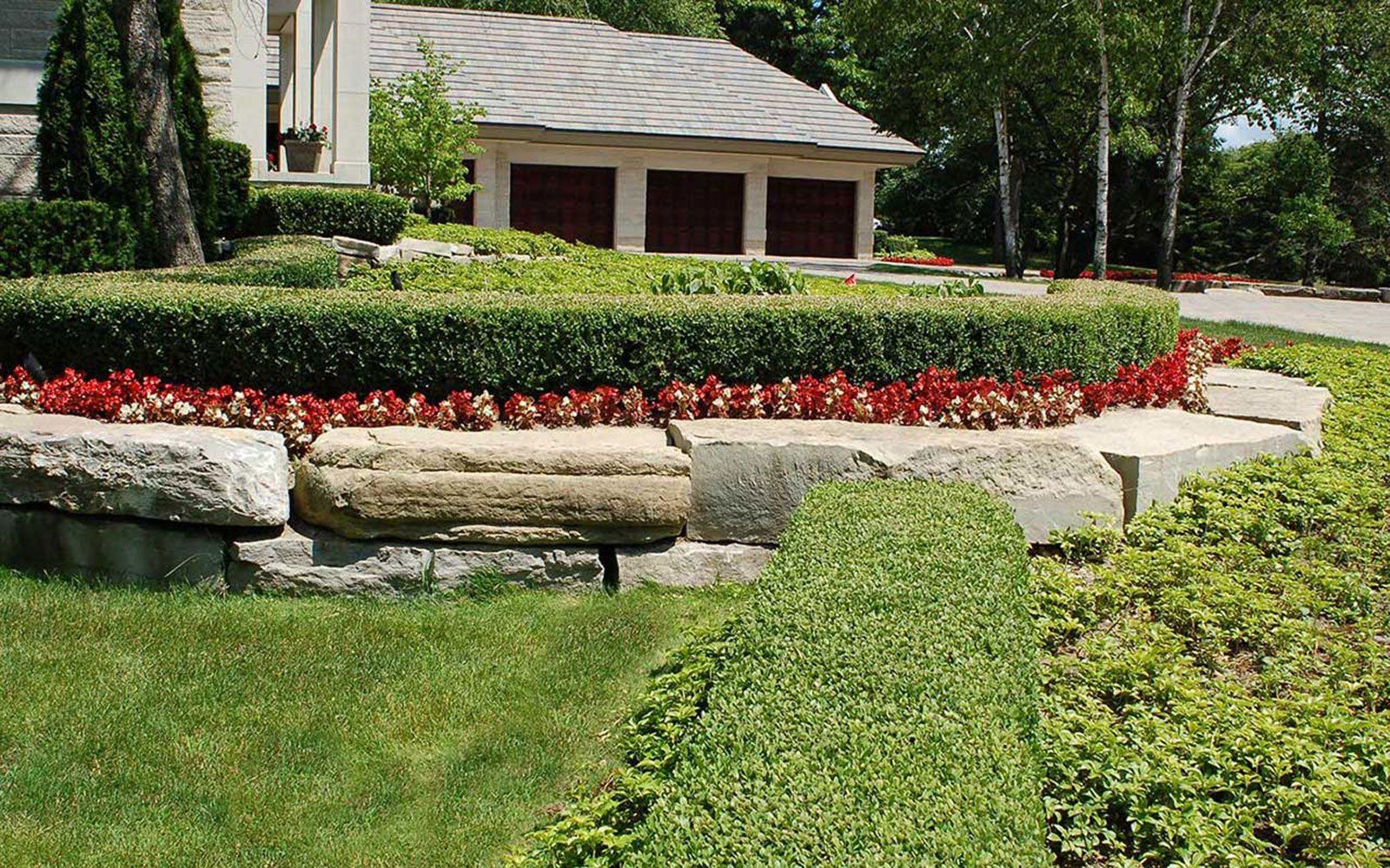 A house with three garage doors is surrounded by a lush green lawn and flowers.