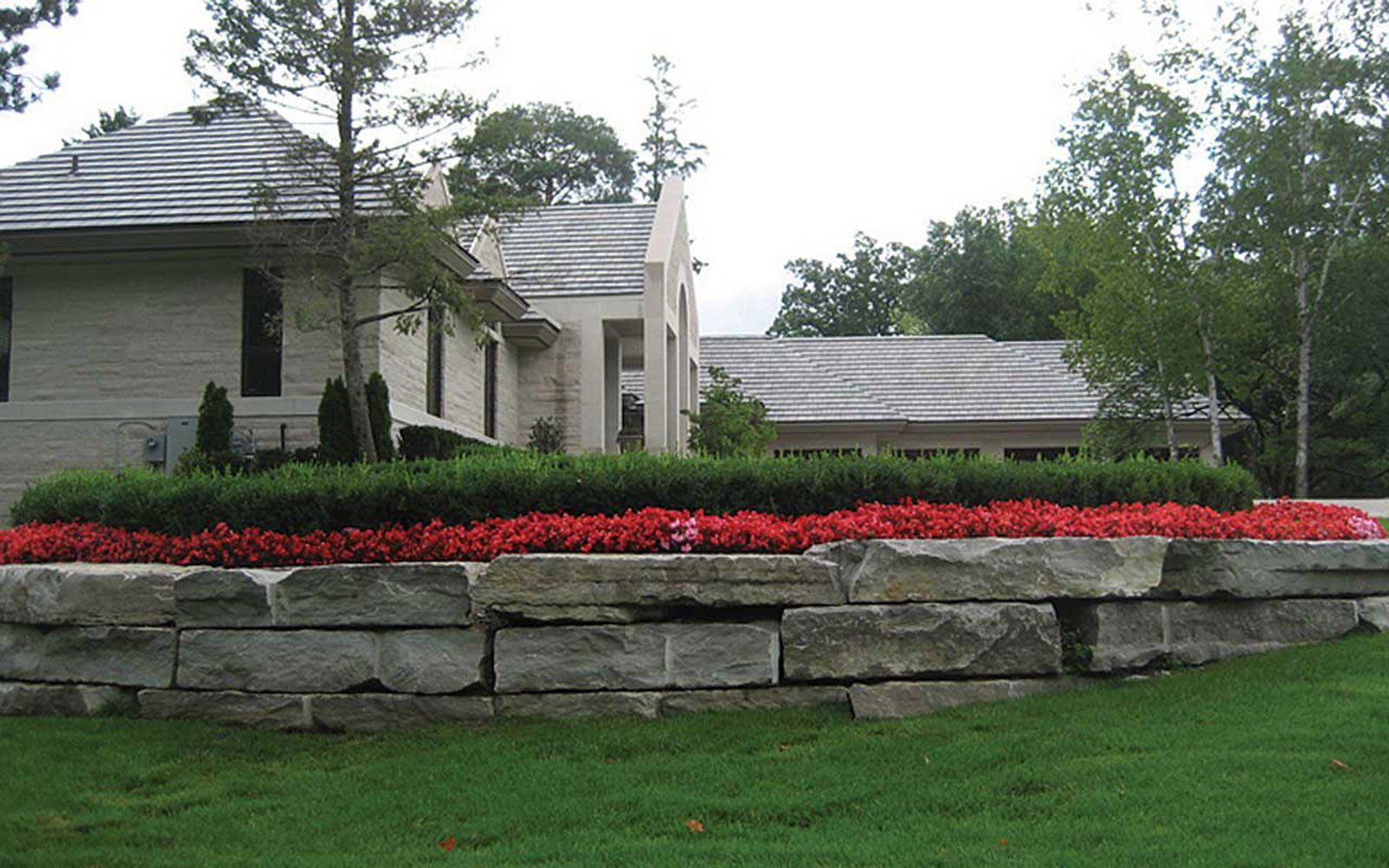 A stone wall with red flowers in front of a house